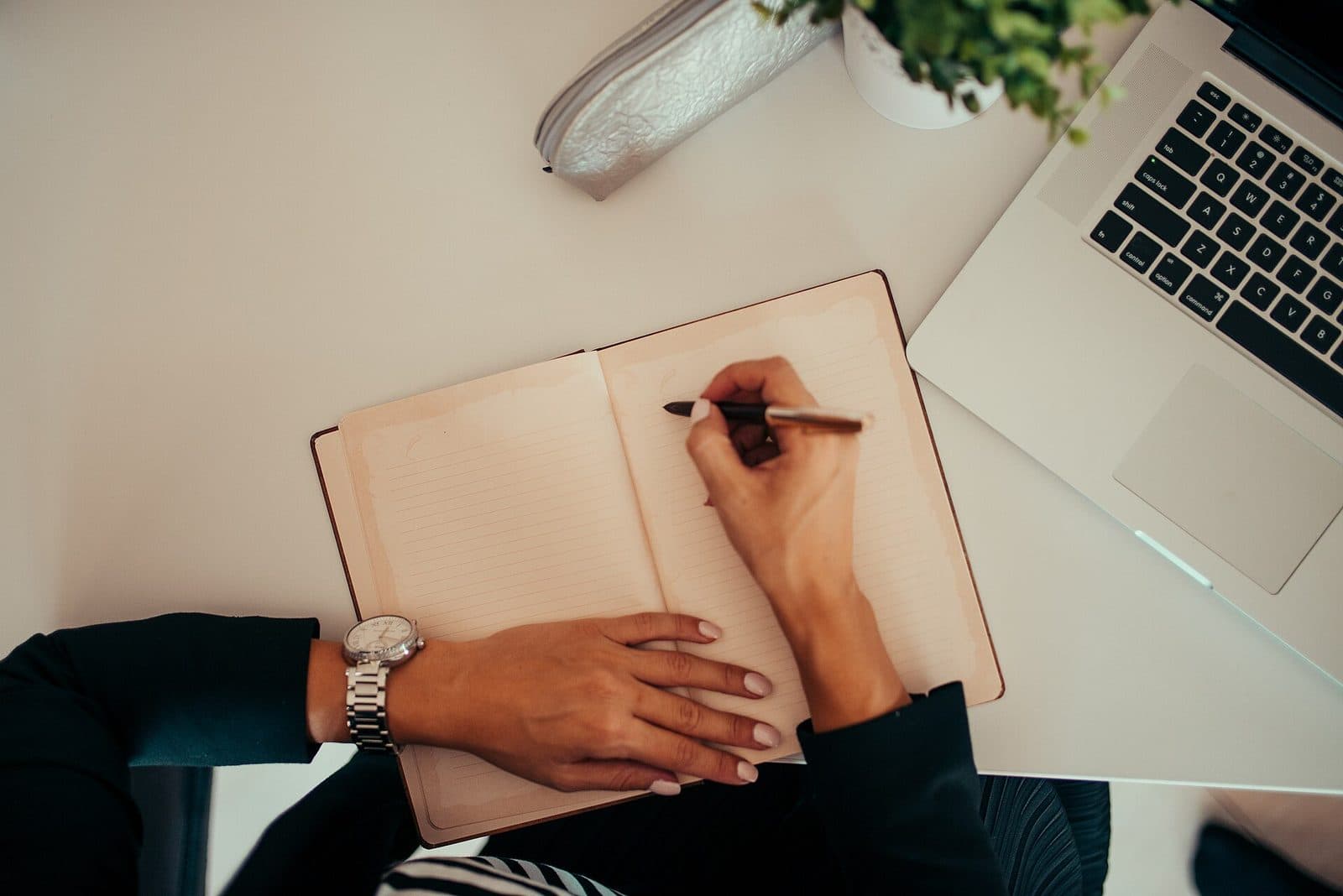 Hands recording source details in a notebook beside a laptop